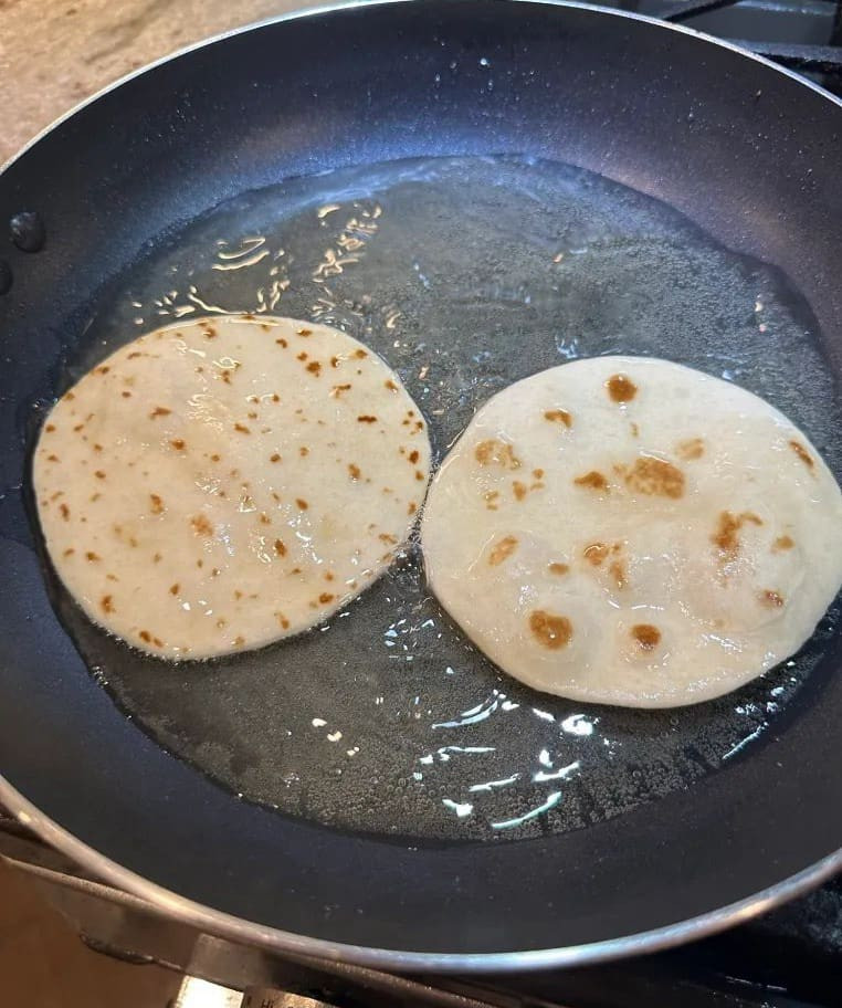 Frying tortillas in hot oil in a skillet, turning golden brown and becoming crispy for Taco Bell Mexican Pizza base.