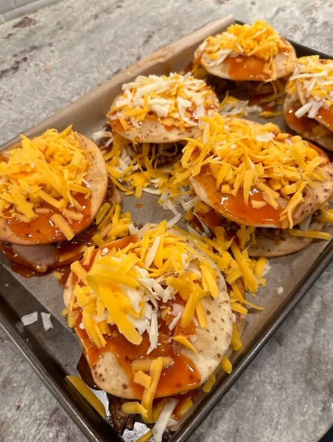 Adding final layers of enchilada sauce and shredded cheese to the top tortilla of Taco Bell Mexican Pizza before baking.
