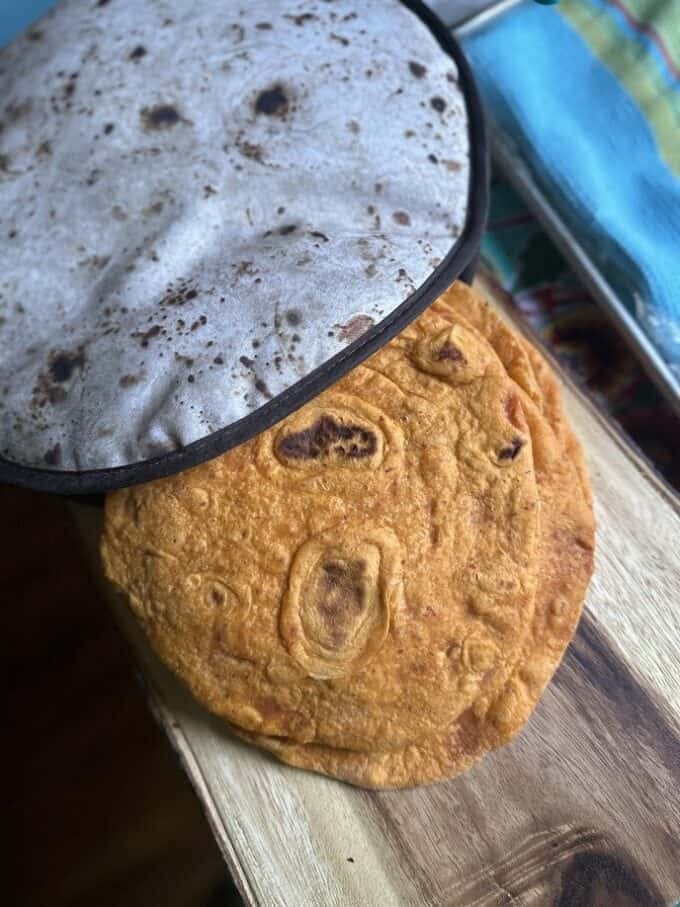 Homemade flour tortillas cooking on a comal, showing golden brown spots and bubbles forming.