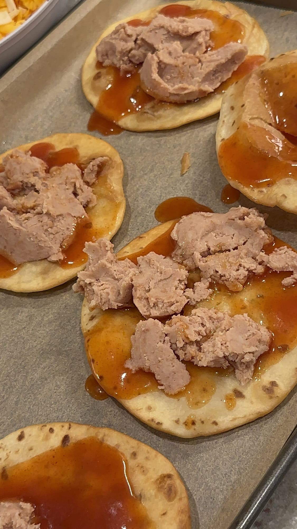 Assembling Taco Bell Mexican Pizza: spreading enchilada sauce and refried beans on fried tortillas.