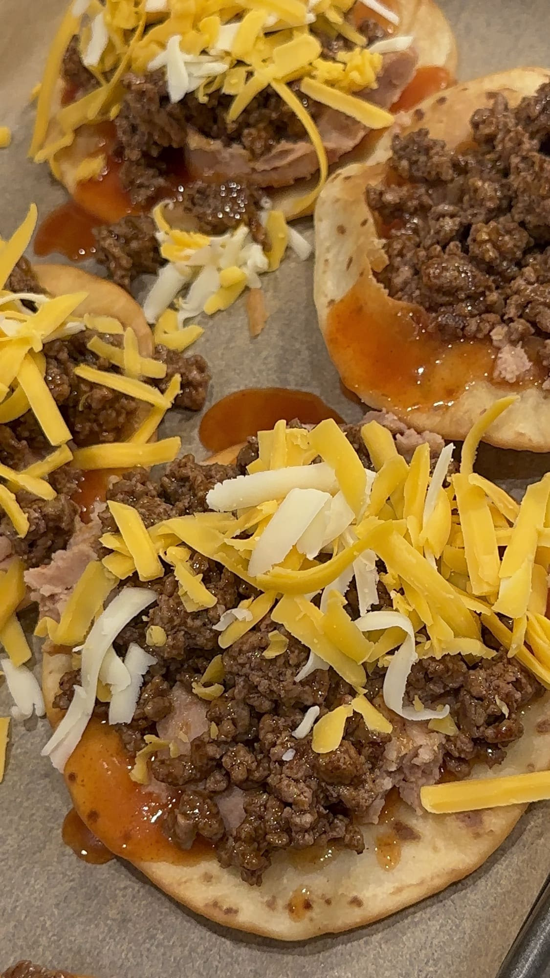 Layering ground beef and shredded cheese on top of refried beans and enchilada sauce for Taco Bell Mexican Pizza.