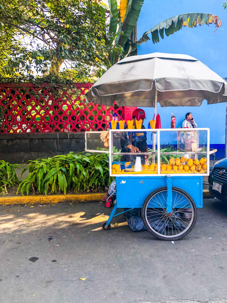 A vendor skillfully preparing a cup of Mexican street fruit, drizzling chamoy sauce over the vibrant mango and other fruits.