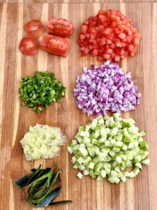 Dicing vegetables for Mexican Shrimp Ceviche, showing hands chopping tomatoes, cucumber, and red onion on a cutting board.