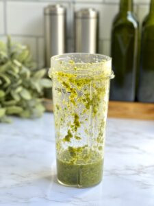 Blending cilantro and serrano peppers with lime juice in a blender, illustrating the preparation of the spicy marinade base.