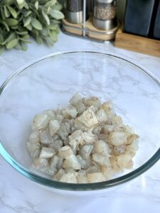 Cutting raw shrimp into smaller pieces on a cutting board, demonstrating the preparation of shrimp for ceviche.