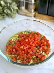 Adding diced tomatoes to the seasoned ceviche mixture, showcasing the incorporation of fresh vegetables.