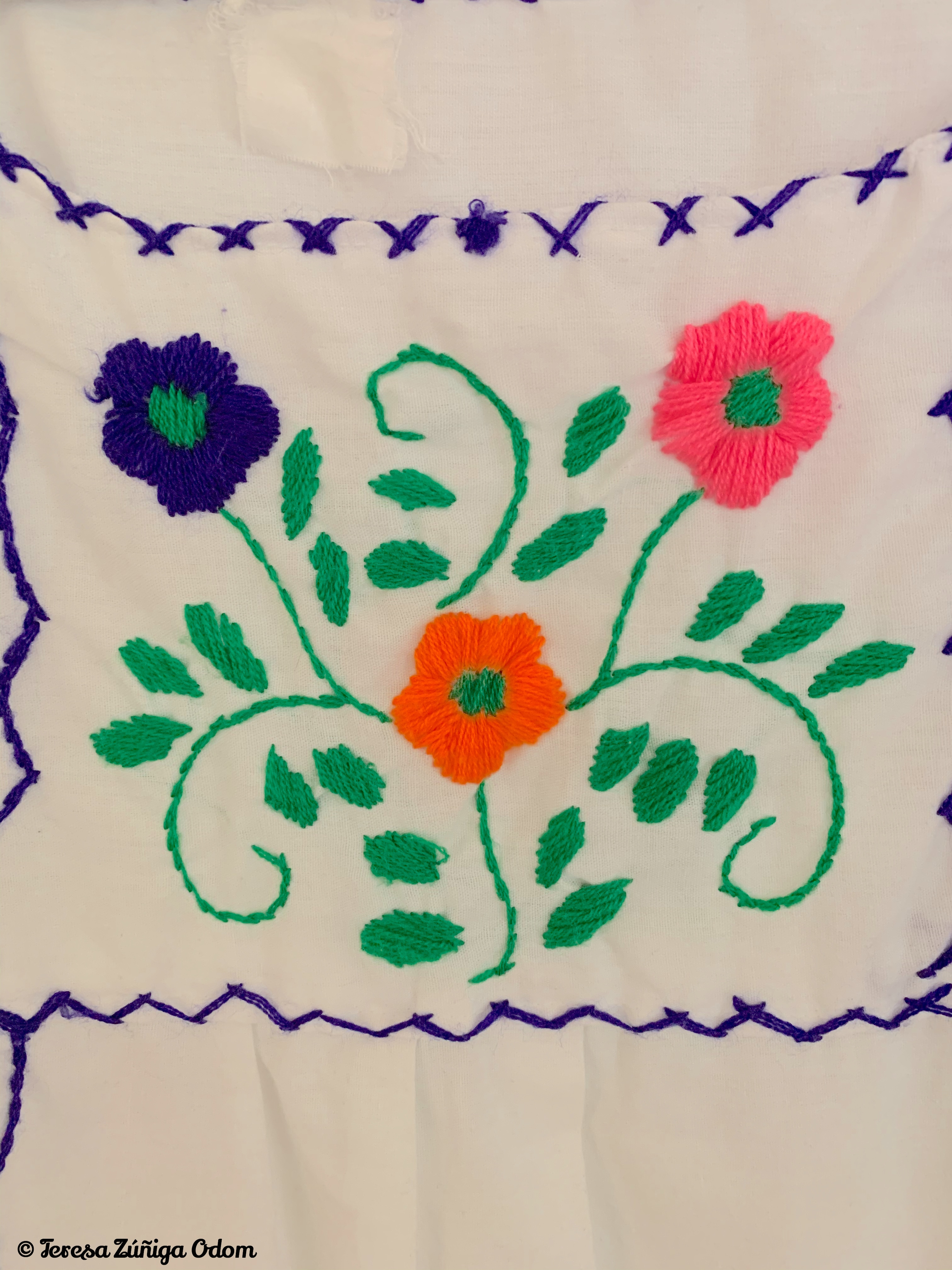 Close-up detail of the multicolored floral embroidery on a white Mexican Puebla dress