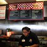 Detailed construction of a Laguna Burger, showcasing layers of ingredients like beef patty, green chile, and cheese, a culinary art in New Mexico.