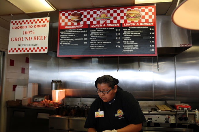 Detailed construction of a Laguna Burger, showcasing layers of ingredients like beef patty, green chile, and cheese, a culinary art in New Mexico.