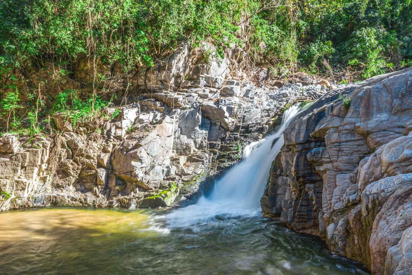A mesmerizing long exposure photograph of Yelapa Waterfall 2 nestled amongst rocks on a bright, sunny day.