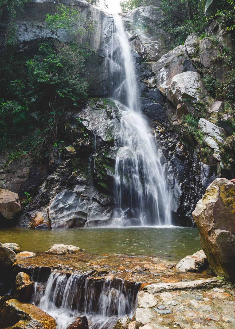 A captivating long exposure shot of Yelapa Waterfall cascading over smooth, dark rocks into its refreshing plunge pool.