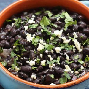 A close up, square image of Mexican black beans in a white bowl, highlighting the texture and fresh cilantro garnish.