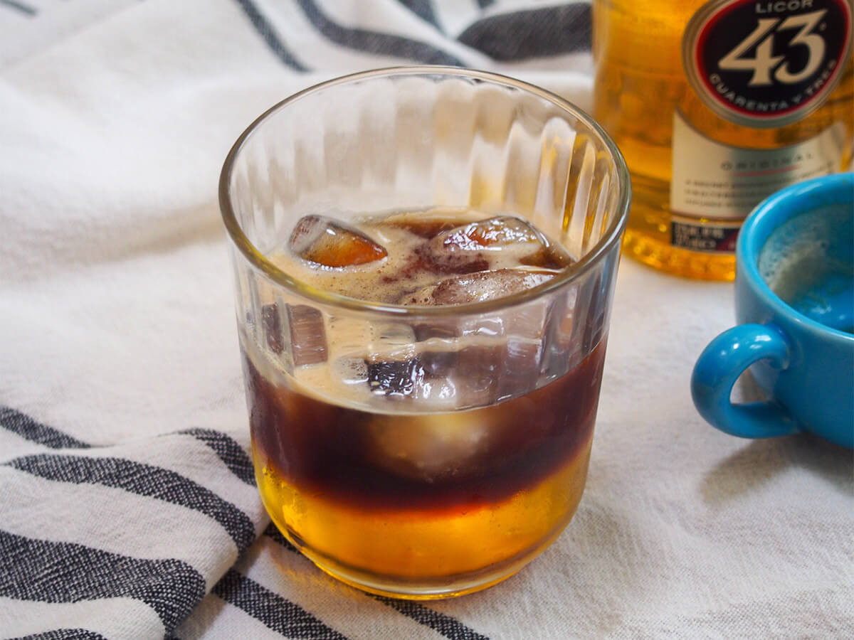 Mexican carajillo coffee cocktail with a bottle of Licor 43 in the background, highlighting the key ingredients.