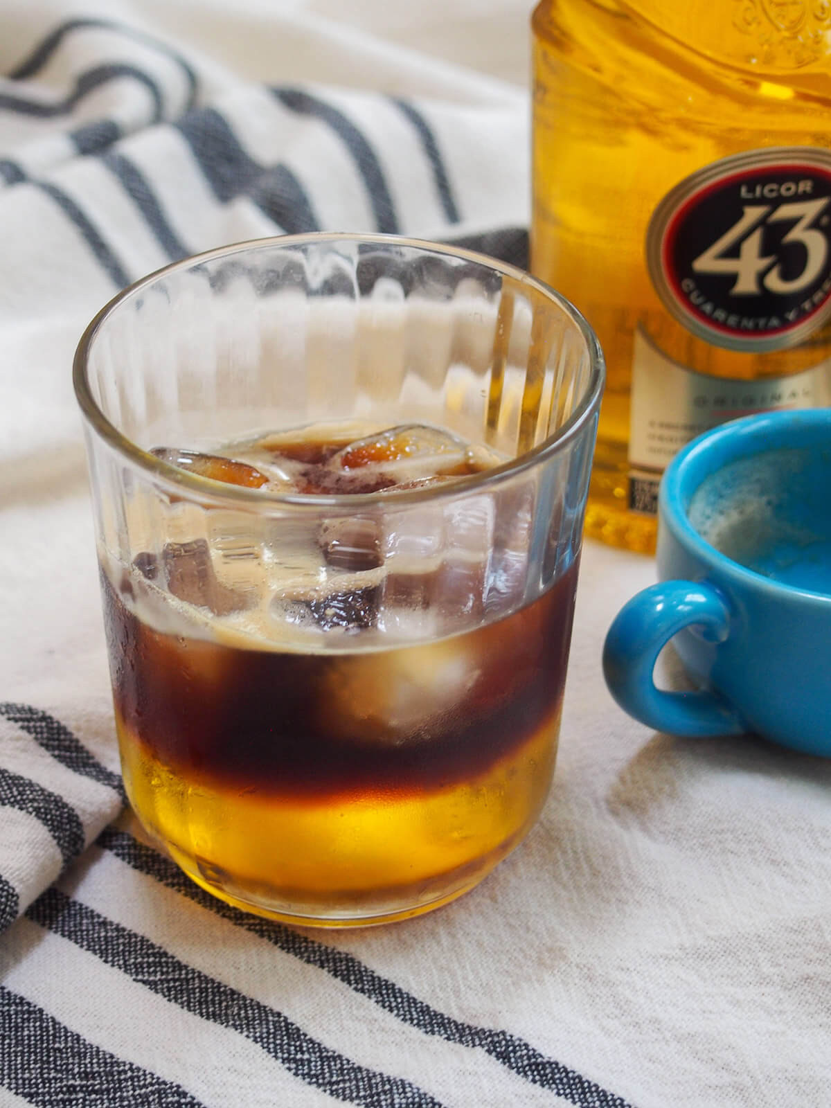 A glass of Mexican carajillo coffee cocktail with an empty espresso cup and bottle to the side, showing the serving style.