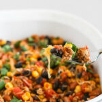 Close up of a fork scooping healthy Mexican casserole from a white dish, recipe title visible above.