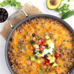 A top-down view of Mexican cauliflower rice in a skillet, garnished with avocado, cilantro, jalapeno, and olives.