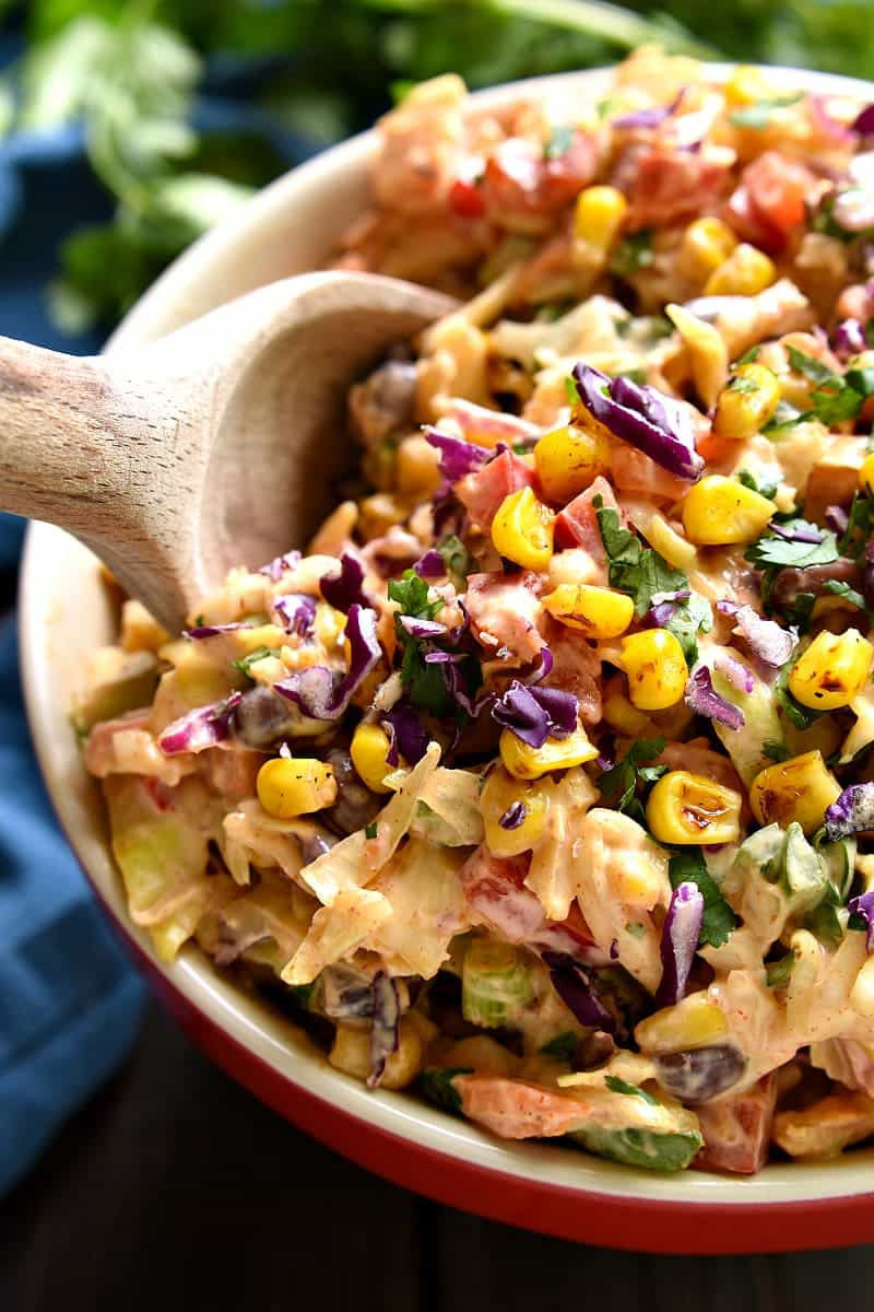 A bowl of Mexican Coleslaw being mixed, showing the vibrant colors and textures of the ingredients before dressing is fully incorporated.