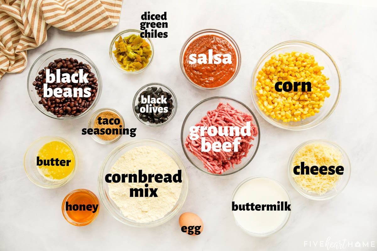 Close-up shot of the ingredients for Mexican Cornbread Casserole, including ground beef, salsa, taco seasoning, beans, corn, olives, cornbread mix, cheese, and green chiles, all laid out on a countertop.
