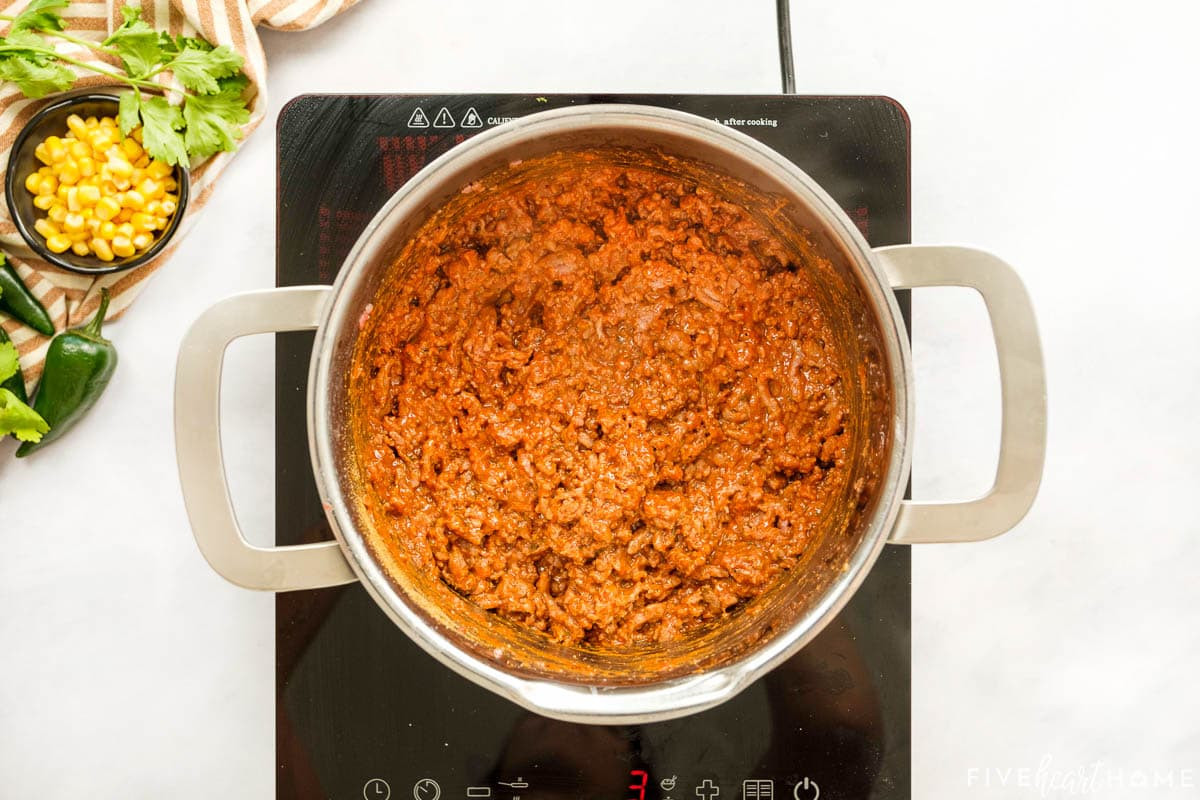 Salsa and taco seasoning being added to the browned ground beef in a pot.