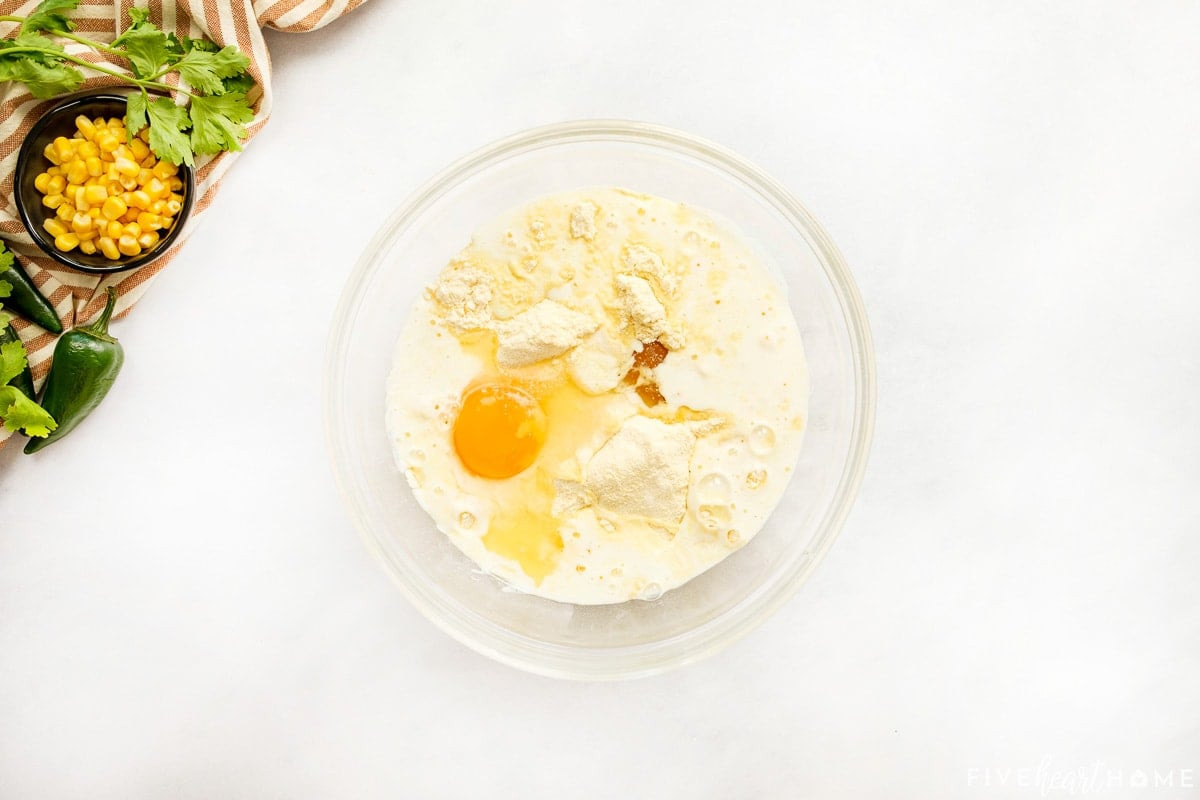 Cornbread batter ingredients in a glass bowl, ready to be mixed.