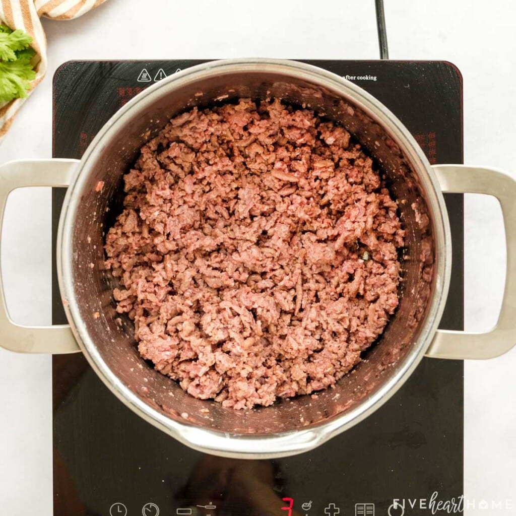 Ground beef being browned in a skillet on the stovetop.
