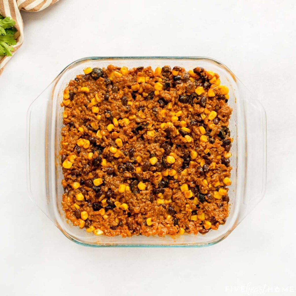 Ground beef filling spread in the bottom of a baking dish, ready for the cornbread topping.