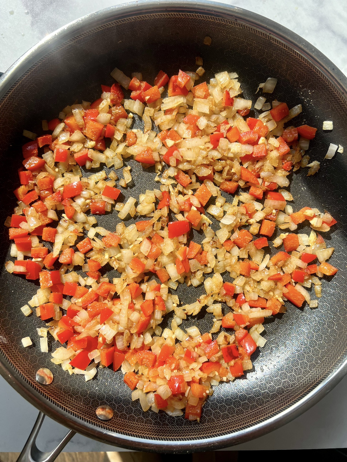 Red bell peppers, onions, garlic and seasonings in sauté pan.