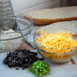 Ingredients for Mexican Garlic Cheese Bread including bread, cheese, mayonnaise, butter, olives, jalapenos, and spices