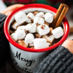 A steaming mug of hot chocolate with Mexican chocolate, topped with marshmallows and a cinnamon stick.