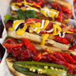 A vibrant and delicious Mexican Hot Dog, showcasing the bacon wrap, grilled toppings, and generous condiments.