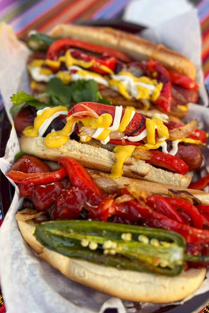 A vibrant and delicious Mexican Hot Dog, showcasing the bacon wrap, grilled toppings, and generous condiments.