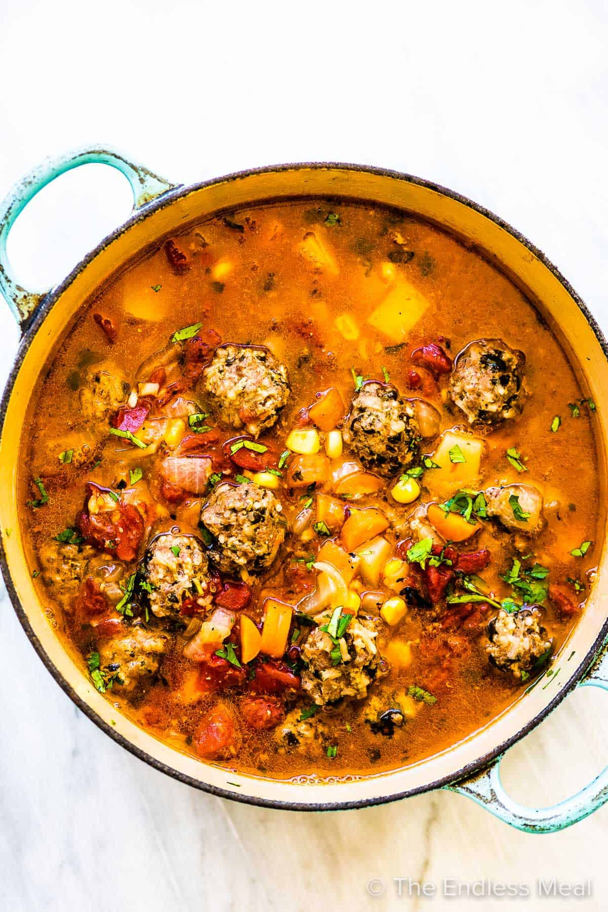 A pot of Mexican meatball soup on a white marble tabletop.