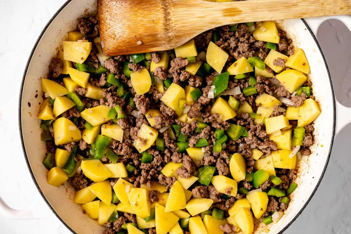 Ground beef, potatoes, onion, and bell pepper cooking in a skillet.