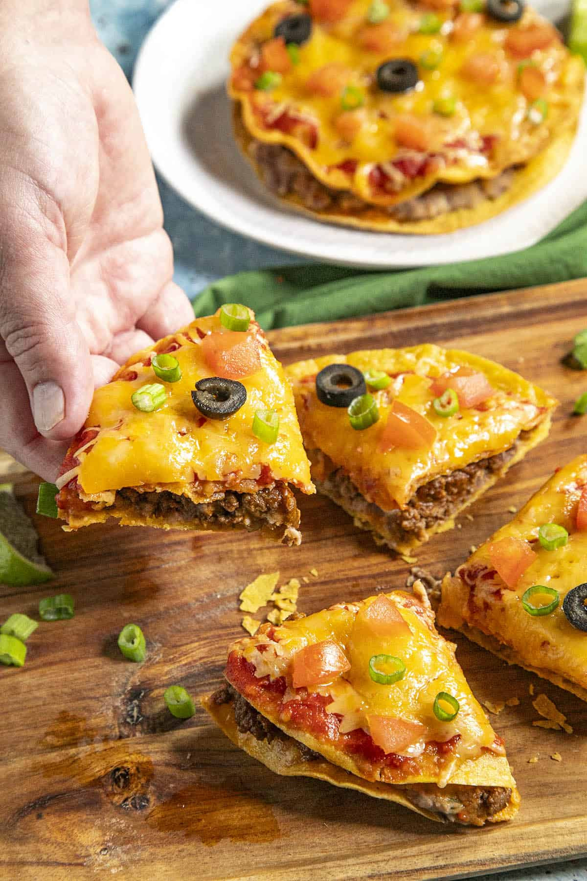 A hand holding a slice of Mexican pizza, showcasing the cheesy, layered texture