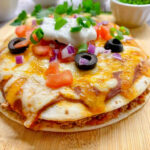 Close-up of a Taco Bell Mexican Pizza copycat on a wooden board, showcasing the layers of tortillas, beans, beef, cheese, and toppings.