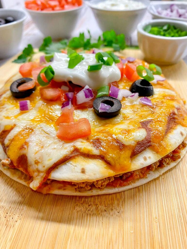 Close-up of a Taco Bell Mexican Pizza copycat on a wooden board, showcasing the layers of tortillas, beans, beef, cheese, and toppings.