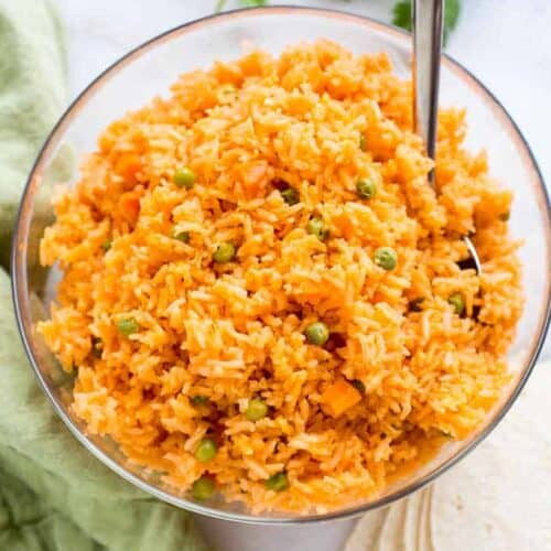 A large bowl of Mexican rice with peas and carrots, served with a spoon.