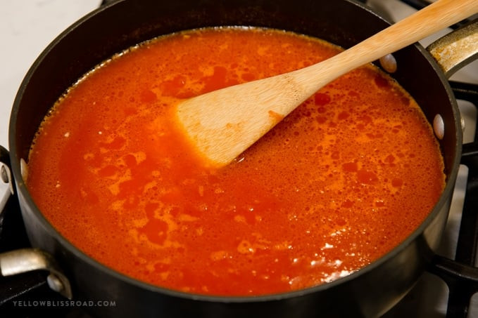 Pouring tomato sauce into the skillet with toasted rice, using a wooden spoon to combine