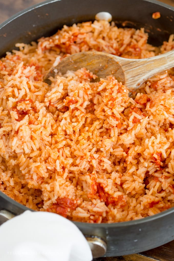 Fluffing perfectly cooked Mexican Rice in a pan with a spoon, showcasing its restaurant-style texture