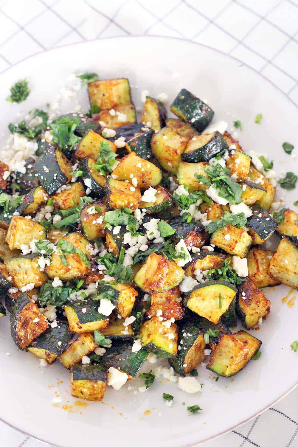 Close-up shot of roasted Mexican zucchini on a plate, showcasing the texture and cotija cheese topping.