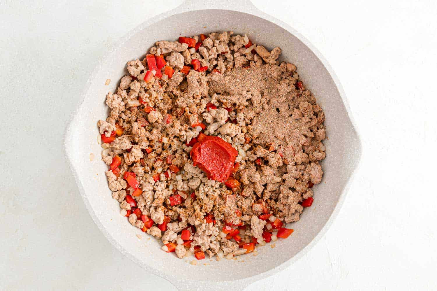 Image showing ground meat, onions, and bell peppers cooking in a skillet, illustrating the sautéing process.