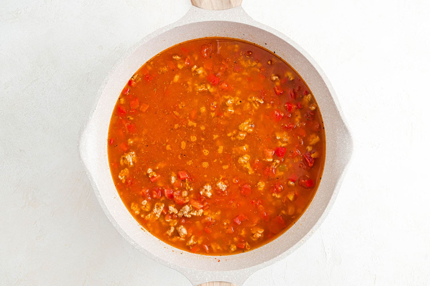 Image of the skillet with all ingredients combined, including water and tomatoes, before bringing to a boil.