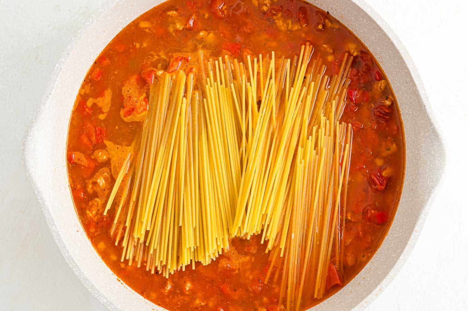 Image showing spaghetti noodles added to the skillet with the sauce, ready to cook.