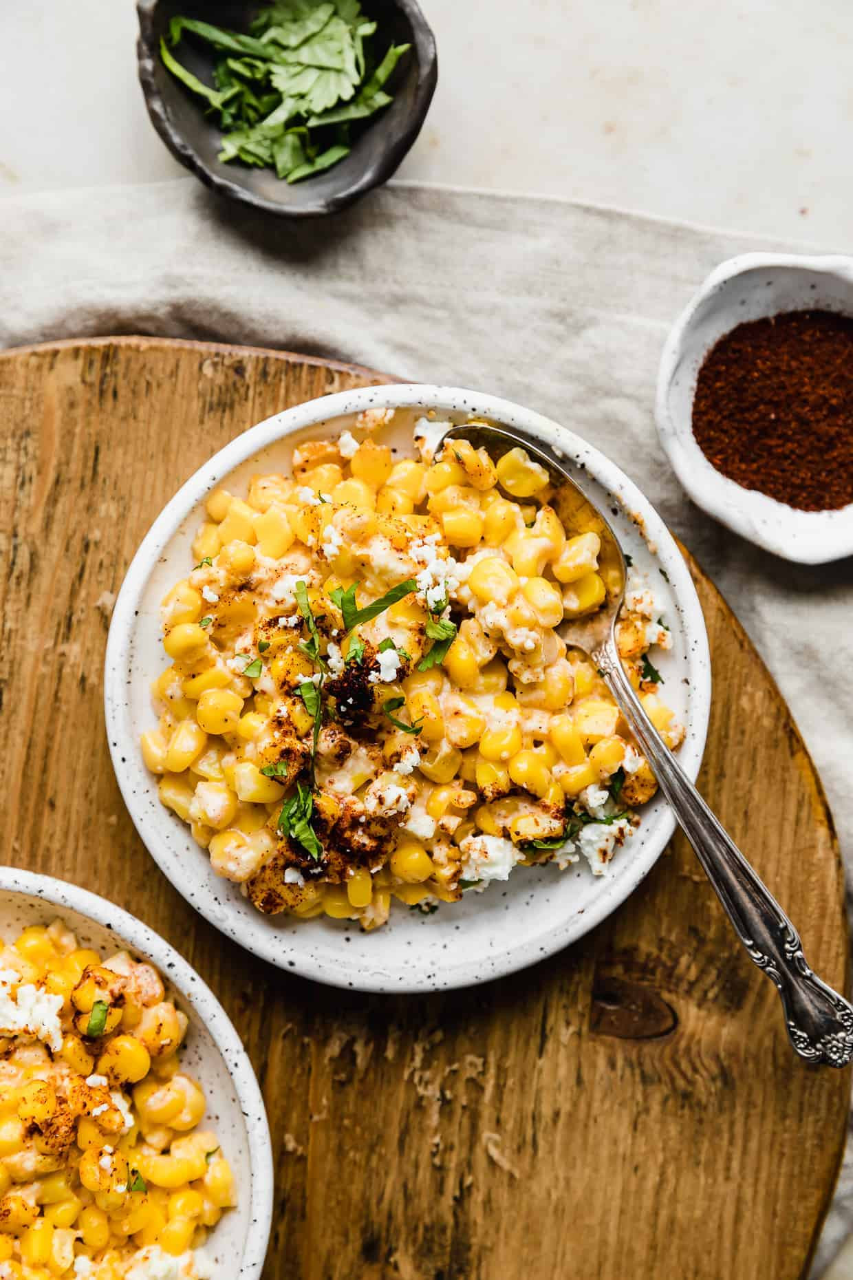 Mexican Street Corn kernels garnished with cilantro and chili powder, served on a white plate against a rustic wooden cutting board, highlighting its vibrant colors and textures.
