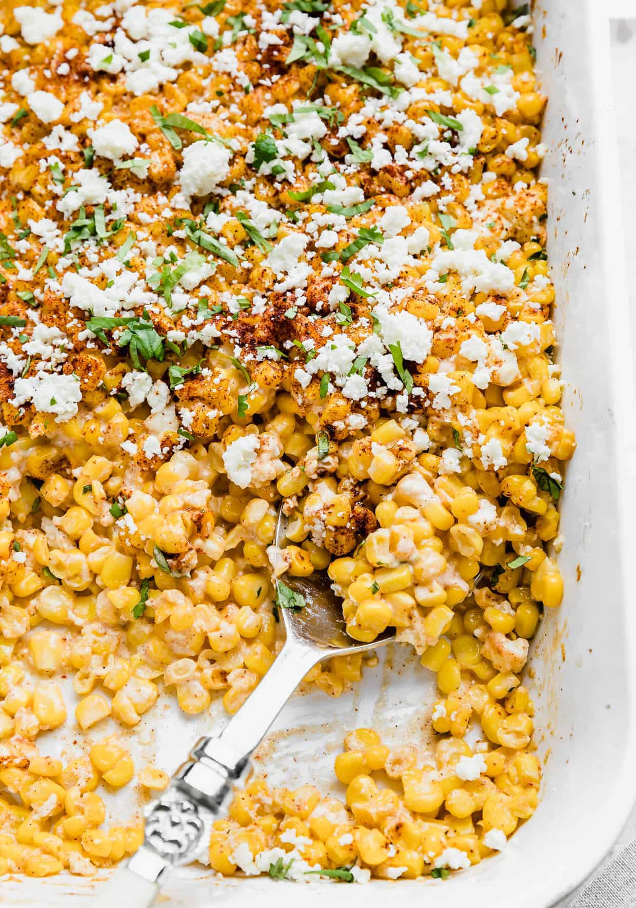 A serving spoon lifting a generous portion of Mexican Street Corn Casserole from a white dish, highlighting its creamy and cheesy consistency.