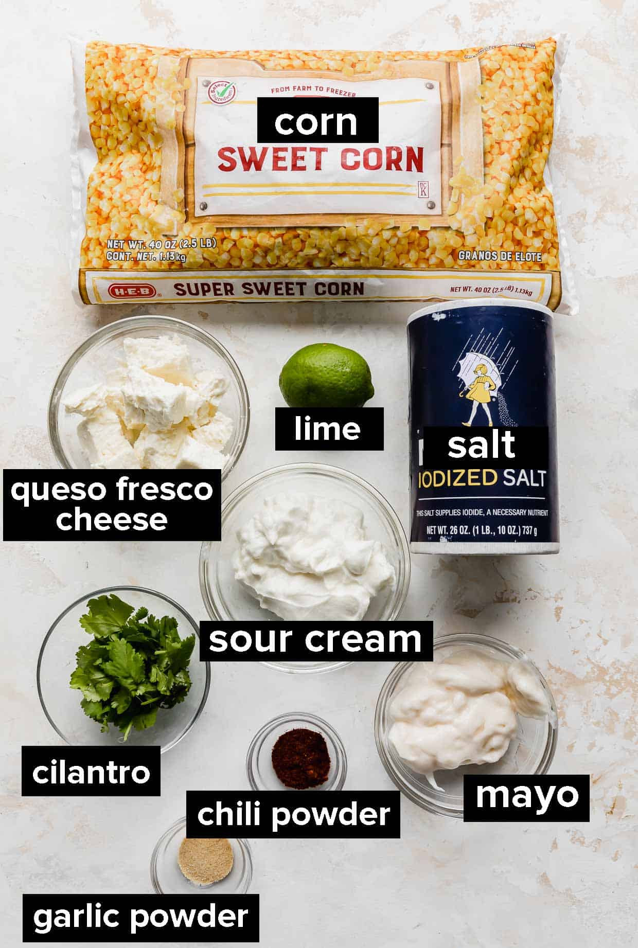 A curated display of ingredients for Mexican Street Corn Casserole, featuring frozen corn, mayonnaise, sour cream, spices, and queso fresco cheese.