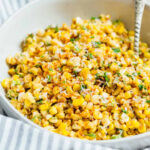 A vibrant bowl of Mexican street corn off the cob, showcasing the charred corn kernels, creamy sauce, and colorful toppings.