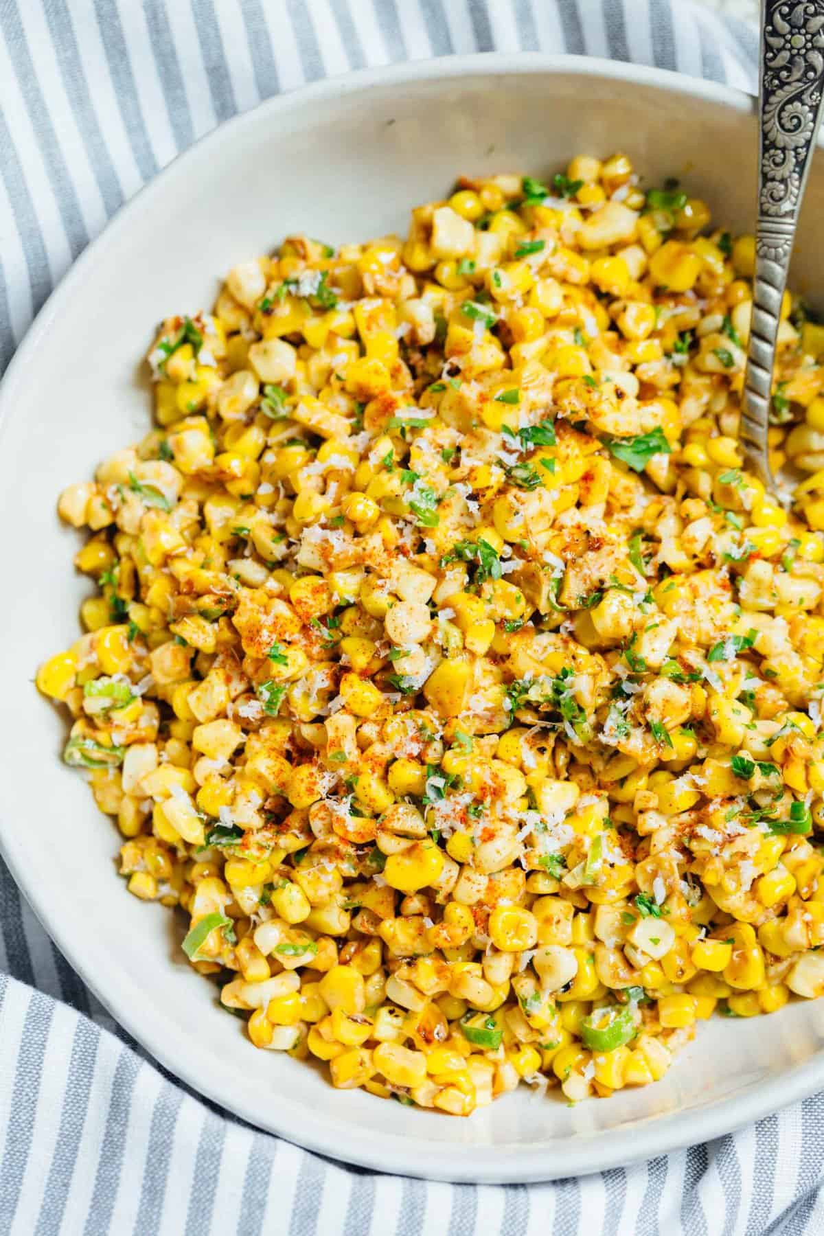 Close-up shot of Mexican street corn off the cob in a white bowl, highlighting the texture of the charred corn and the creamy sauce.