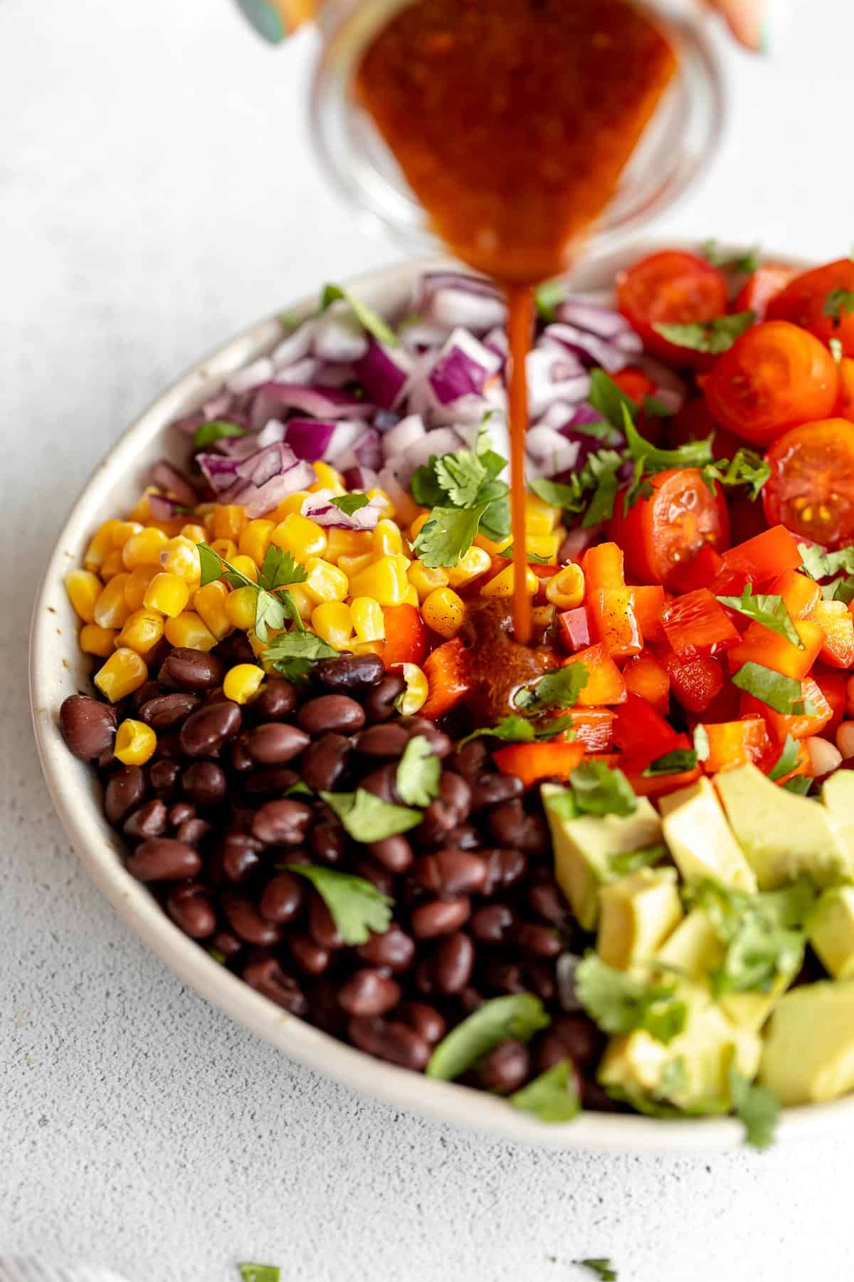 Pouring the flavorful and spicy dressing over the colorful Mexican bean salad in a large bowl