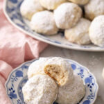 A plate of Mexican wedding cookies, with one cookie on top having a bite taken out to show the texture.